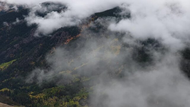Aerial of mountain slopes with autumn foliage and low clouds moving through valleys near Crested Butte South Colorado