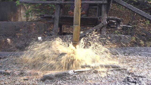 Traditional crude oil extraction using a pipe bailer at Teksas Wonocolo traditional oil field in Bojonegoro, East Java, Indonesia. Manual petroleum mining process from deep well with raw oil splash.