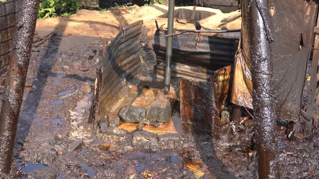 Traditional crude oil extraction using a pipe bailer at Teksas Wonocolo traditional oil field in Bojonegoro, East Java, Indonesia. Manual petroleum mining process from deep well with raw oil splash.