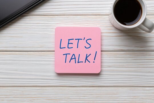 Note with pink sticky message lets talk on wooden office desk with coffee for business work
