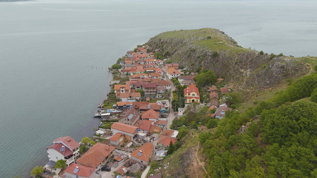 Aerial view of the village of Lin on a peninsula in Lake Ohrid, featuring traditional houses with red-tiled roofs, a church, and lush green hillsides, Lin, Korce County, Albania.