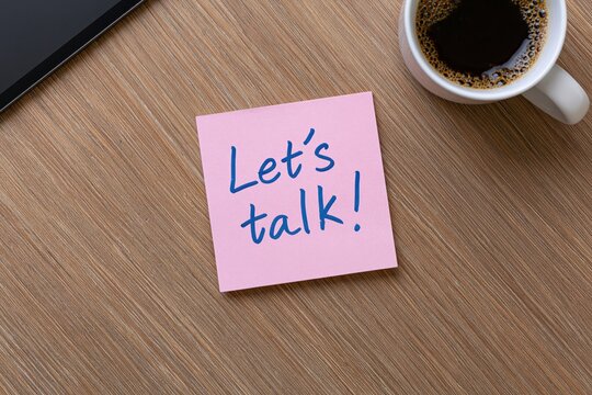 Note with sticky pink paper message let us talk on a wooden office desk with a cup of coffee