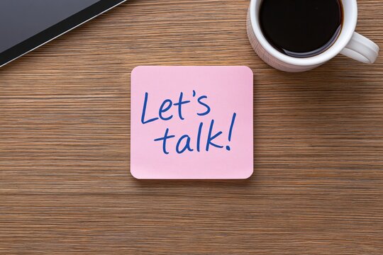 Note with sticky pink message lets talk handwritten on a wooden office desk with a smartphone