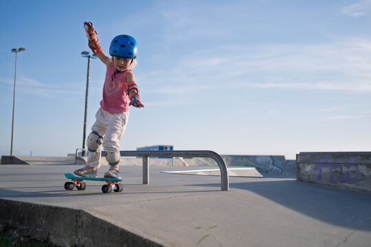 Little Girl in Helmet and Protective Gear Balancing on Penny Board at Skatepark