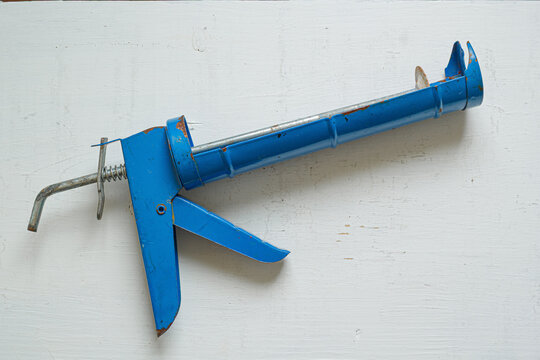 An old, blue caulking gun rests on a weathered white wooden surface.