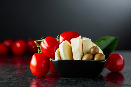 Mozzarella with green olives and red cherry tomatoes on a black stone table.