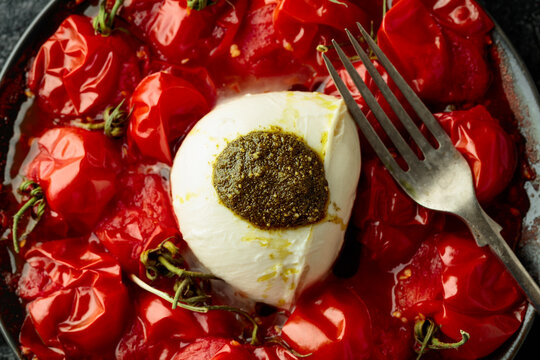 Mozzarella with pesto sauce and roasted red cherry tomatoes on a black plate.