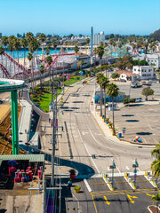 Fototapeta premium Aerial shot reveals the amusement park attractions, roller coasters, palm trees, and roadway adjacent to the coastline at Santa Cruz Beach Boardwalk in California.