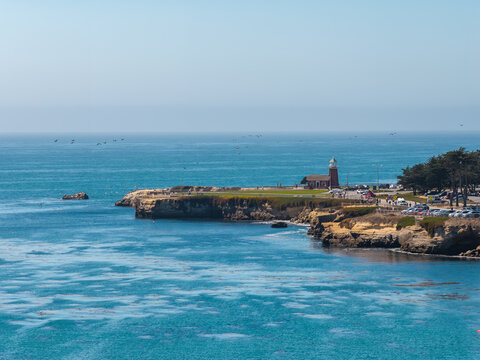 Aerial perspective of Lighthouse Point and Mark Abbott Memorial Lighthouse in Santa Cruz, California, surrounded by the Pacific Ocean coastline, sandstone cliffs, and open water on a sunny day.
