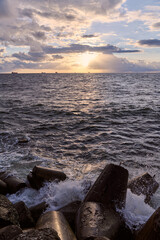Fototapeta premium Ocean waves break against coastal barriers beneath golden sunset light
