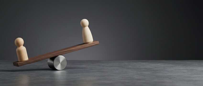 Concept of imbalance and inequality featuring two wooden human figures on a wooden seesaw scale balanced over a metal cylinder against a dark grey background with ample copy space.