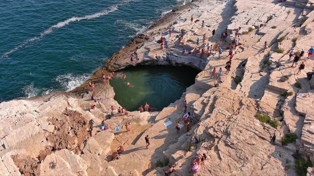 Aerial view of the natural rock pool Giola with people swimming in turquoise water surrounded by rugged cliffs along the coastline of Thasos, Greece.