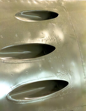 Close-up of machinegun openings on a silver colored old fighter jet 
