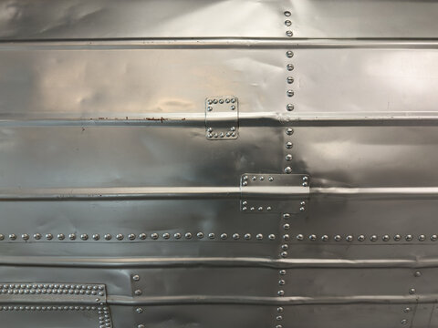Close-up macro of bright silver colored metal wall with lines of rivets
