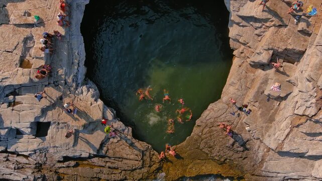 Aerial view of people swimming in the natural rock pool of Giola Lagoon surrounded by rugged cliffs in Thasos, Greece.