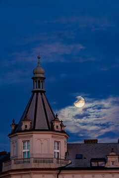 A scene at dusk as the moonlight breaks through the blue clouds and illuminates the rooftop with the tower. Prague, Czech Republic 