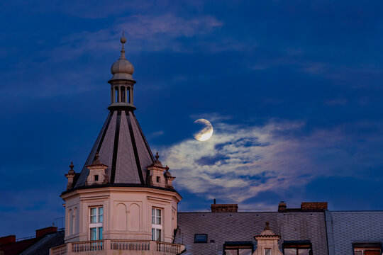 The moon over the roof of the historical building during the evening. Prague, Czech Republic 
