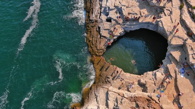 Aerial view of the Giola natural pool with people swimming in the turquoise water surrounded by rocky cliffs in Thasos, Greece.