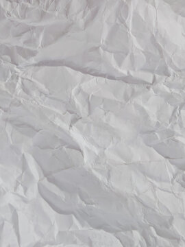 Close up full frame macro photograph of a crumpled piece of white paper. The wrinkled, crushed document provides a textured, high-key background