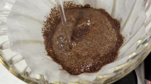 Close up pouring hot water on ground coffee beans in V60 filter dripper
