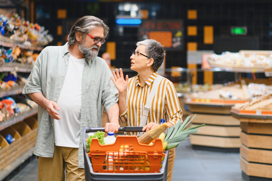 Senior couple shopping groceries discussing in supermarket aisle
