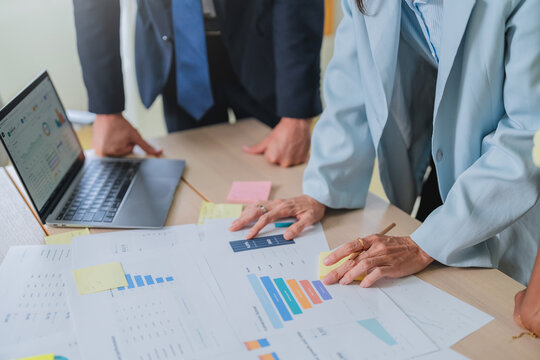 overhead shot of a business team's hands pointing at financial charts on a tablet, surrounded by printed reports and sticky notes. This detailed scene captures collaborative data analysis and strategi