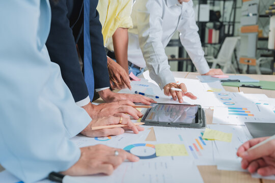 overhead shot of a business team's hands pointing at financial charts on a tablet, surrounded by printed reports and sticky notes. This detailed scene captures collaborative data analysis and strategi