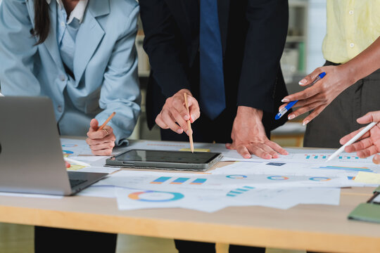 Multiple colleagues point and gesture around printed reports, a laptop, and tablet during an intense strategy session. This dynamic detail shot reflects teamwork, financial planning, and hands-on busi