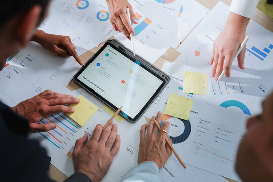 overhead view of a business team analyzing charts and data spread across a table, with a tablet displaying a SWOT analysis. This detailed shot captures strategic planning, collaboration, and data-driv