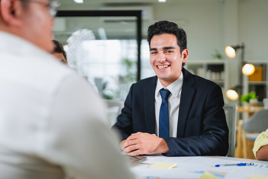 businessman smiles warmly while listening attentively during a meeting, hands clasped on the table. This candid portrait captures active engagement, confidence, and positive professional communication