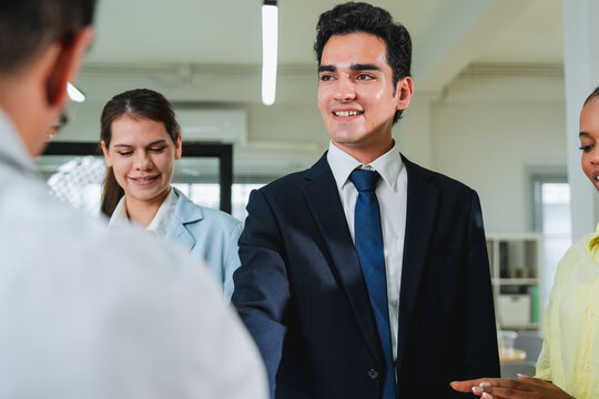 businessman stands smiling among diverse colleagues in a casual office gathering, shot from a low, dynamic angle. This candid group moment captures camaraderie, workplace culture, and confident social