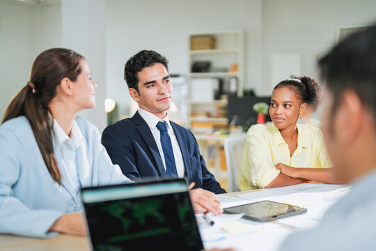 diverse team collaborates during a business meeting, smiling and engaged around a laptop displaying data charts. This candid office moment captures teamwork, professionalism, and positive workplace co