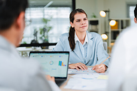 businesswoman listens attentively during a meeting, with colorful data charts visible on a laptop screen in the foreground. This focused portrait captures analytical thinking, professionalism, and eng