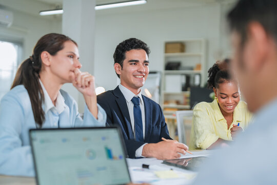 diverse team collaborates during a business meeting, smiling and engaged around a laptop displaying data charts. This candid office moment captures teamwork, professionalism, and positive workplace co