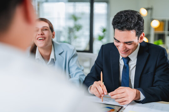 diverse team collaborates during a business meeting, smiling and engaged around a laptop displaying data charts. This candid office moment captures teamwork, professionalism, and positive workplace co