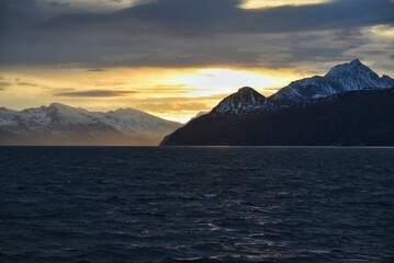 Golden sunset sky over dark ocean waves and snow covered mountain peaks  © youness