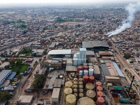 Aerial view of an industrial facility featuring large storage tanks and factory buildings with smoke rising from chimneys, situated within the urban landscape of Multan, Punjab, Pakistan.