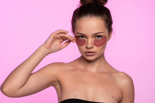 Young woman applying pink hydrating eye patches for a cosmetic skin treatment, promoting beauty and self-care