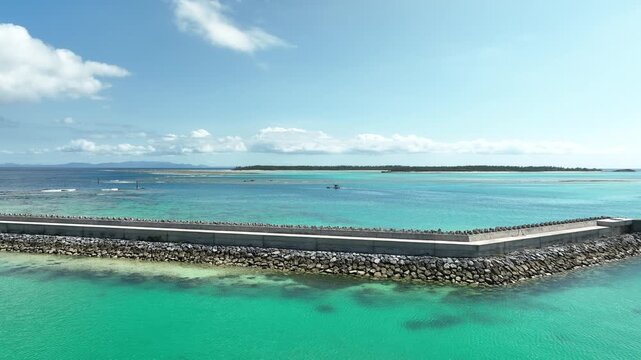 伊是名島の漁港からエメラルドグリーンの海を越えて沖へ進むドローン空撮
