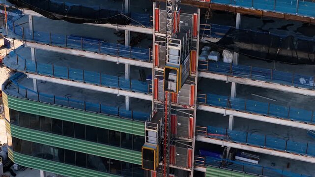 Aerial view of a construction site with a vertical lift elevator and green facade panels at Kendall Square in Cambridge, Massachusetts, United States.
