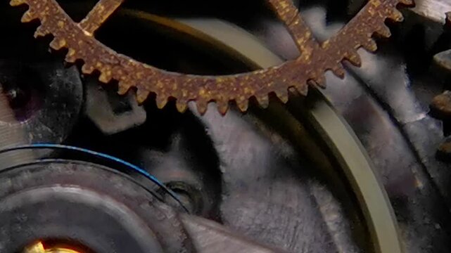Ultra macro footage of an antique mechanical watch mechanism showing oxidized rusty brass gear, oscillating balance wheel, and expanding blue hairspring in motion.