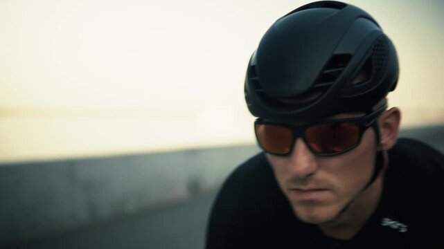 Cyclist Wearing Helmet And Sunglasses Riding Bicycle Road Racing Training Outdoors. Biker Cycling Fast On Highway Street During Sunset