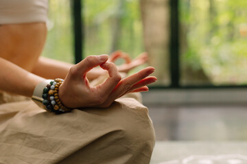 young woman practices yoga and meditation in a room with large windows, with a forest in the background, in the summer