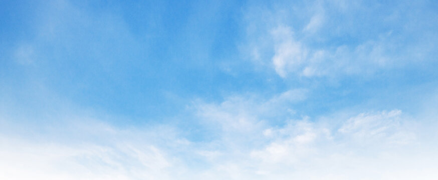Soft clouds drift across a serene, light-blue sky
