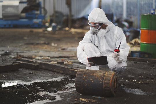 
Worker in full hazmat suit inspects rusty barrel