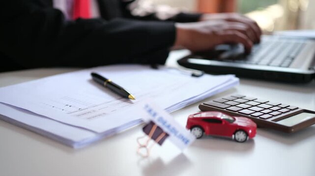 A "DEADLINE" sign clipped to a document sits on a busy desk, set against a backdrop of office workers typing away on their laptops. It represents a target that must be met before the due date&mdash;a race a