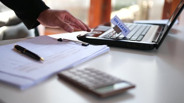 A hand placing an "ON LEAVE" sign on a keyboard. Concept of taking a break from work, annual leave, holidays, or family time.

