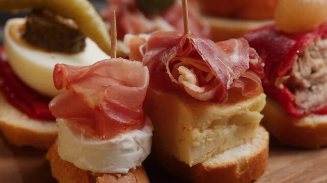 Tapas Spanish pinchos assortment, Basque pintxos with jamon iberico, tortilla, shrimp, stuffed piquillo pepper and egg on bread, traditional bar food close up