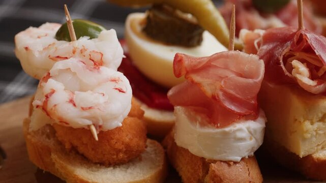 Tapas Spanish pinchos assortment, Basque pintxos with jamon iberico, tortilla, shrimp, stuffed piquillo pepper and egg on bread, traditional bar food close up