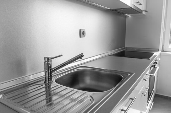 A modern kitchen featuring a stainless steel sink, sleek faucet, metallic backsplash, and polished countertops.